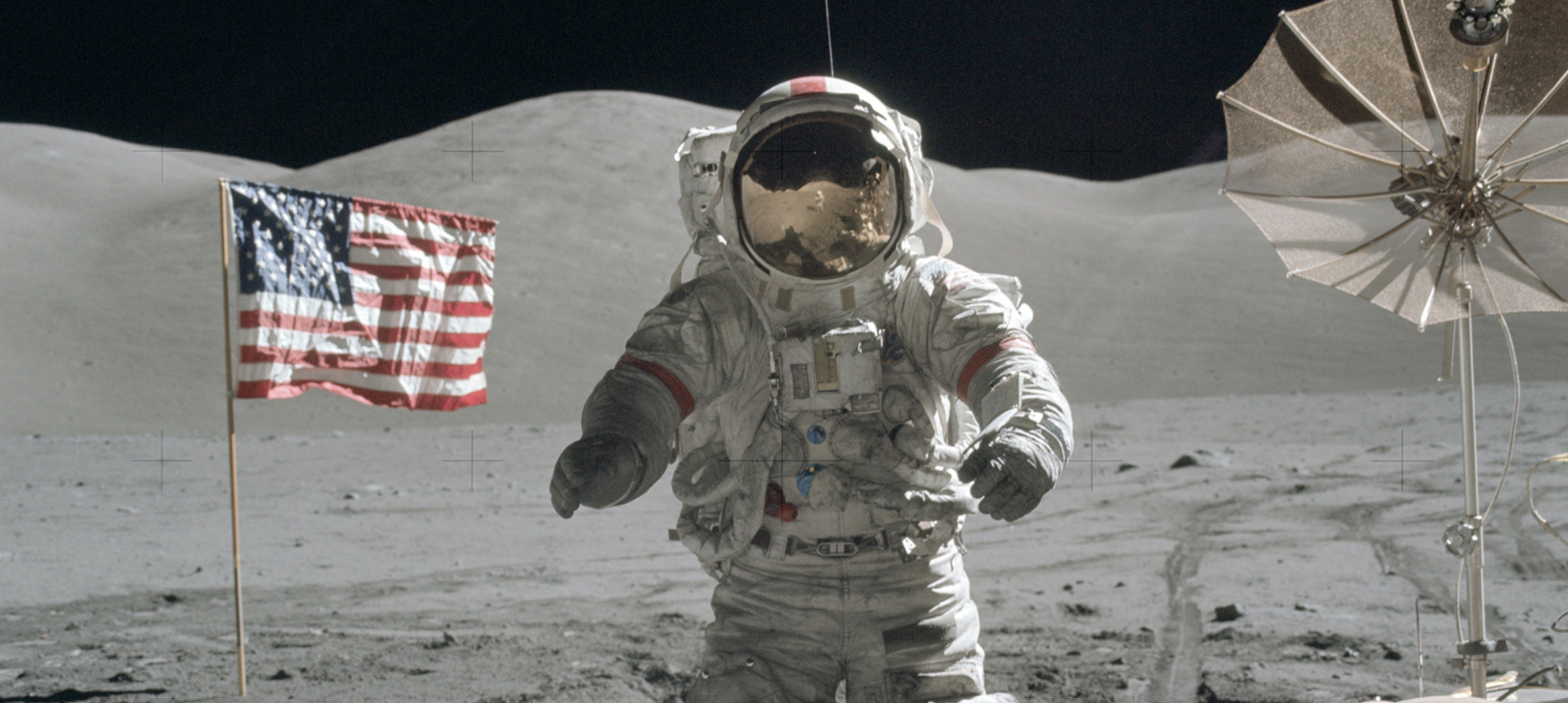 Astronaut in white spacesuit walking on lunar surface with American flag