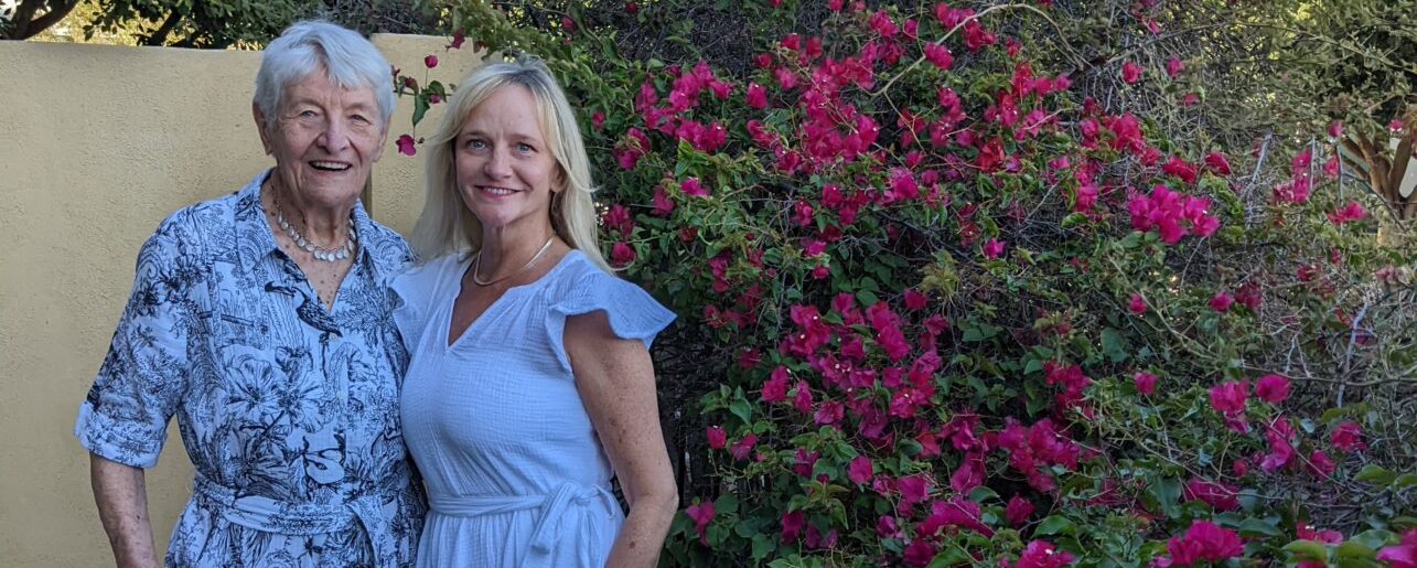 Two women smiling together in front of vibrant magenta flowering vines